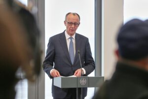 Linke und Grüne empört über Merz-Rüstungspläne mit Golfstaaten Friedrich Merz spricht am Pult, kritische Reaktionen zu Waffenexporten im Hintergrund sichtbar.